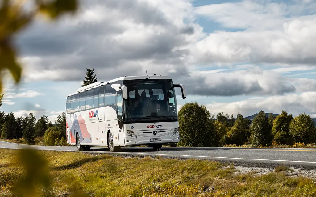 valdresekspressen står på en asfaltert vei med grønt gress og blader i forgrunnen