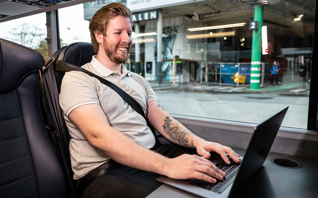 Mann sitter med pc på buss og jobber