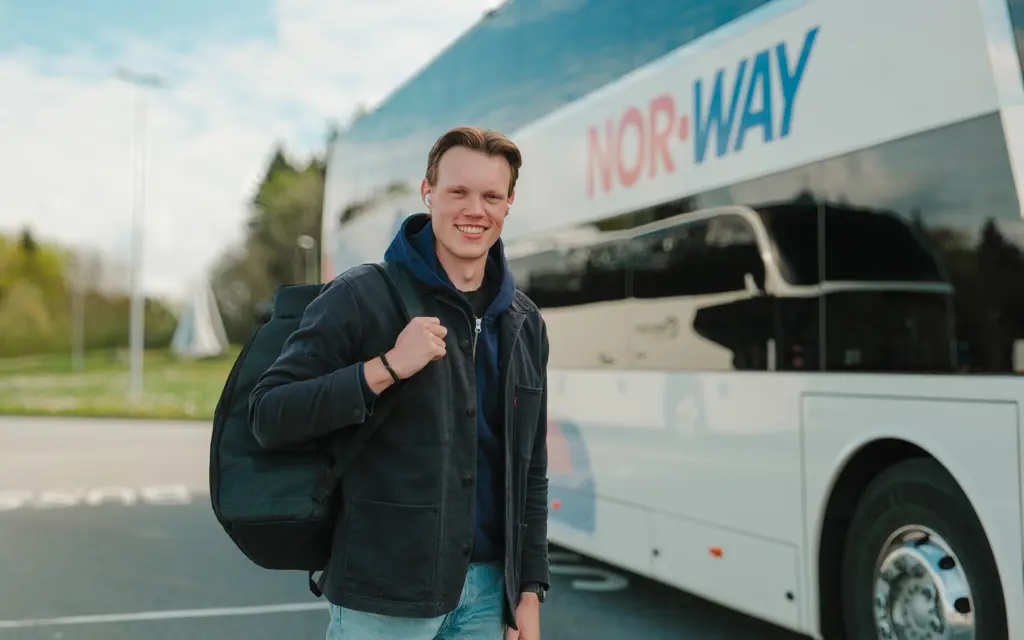 Smilende student med ryggsekk utenfor NOR-WAY buss