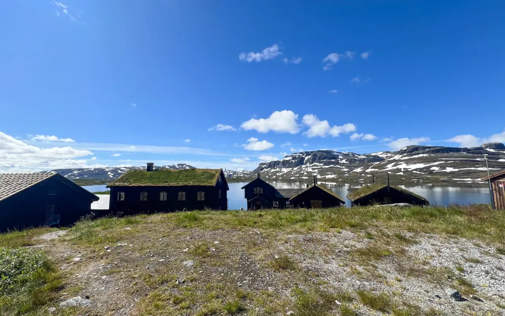 DNT-hytta Haukeliseter i solskinn, med blå himmel og små snøpartier på fjellene i bakgrunnen